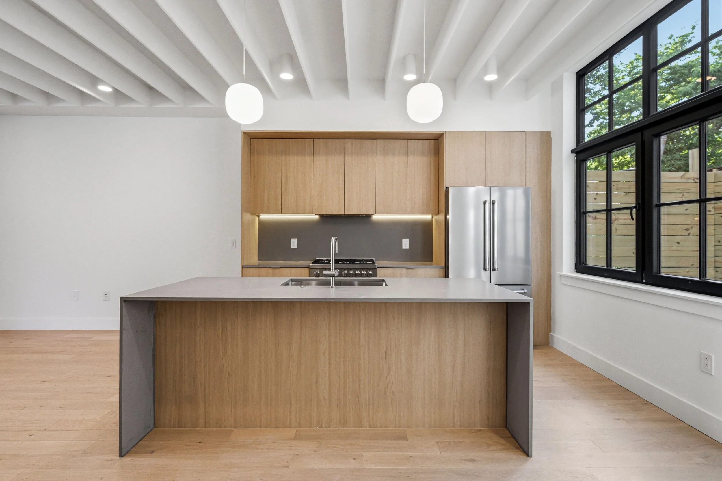 Wildey Street kitchen with warm oak cabinetry, a stone waterfall island, globe pendant lights, and large black-framed windows